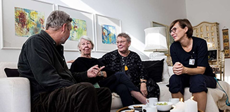 Tre kvinder og en mand sidder sammen i en sofa omkring et kaffebord