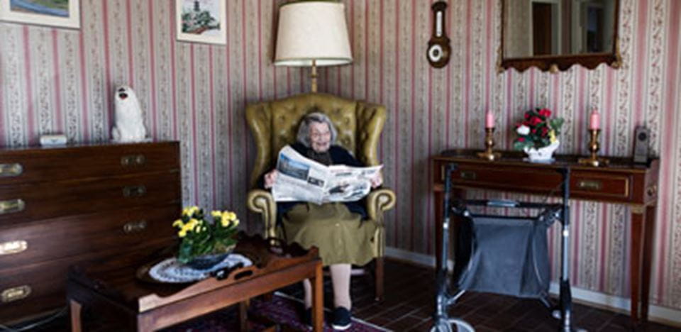 Ældre kvinde sidder og læser avis i sin stue